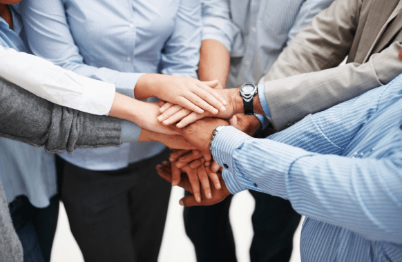 A photograph of people standing in a circle all piling hands in the center.