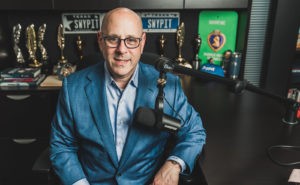 A photo of Kevin Hodes smiling in front of a microphone. 