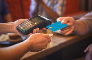 A picture of someone handing a blue credit card to a person with a card reading machine.