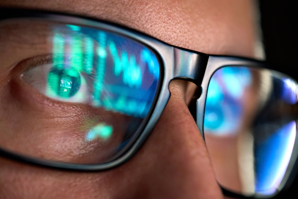 A closeup photo of a person wearing glasses with the reflection of a computer screen on them.